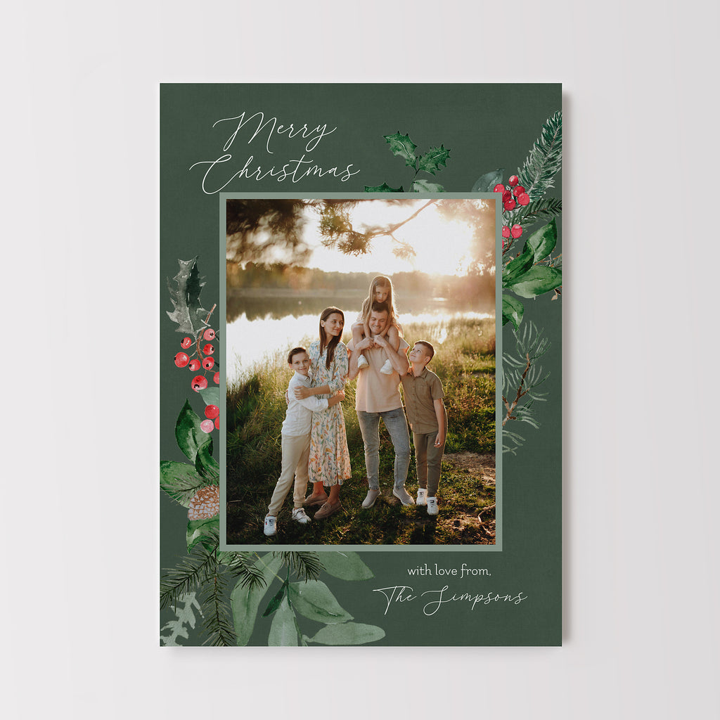 Holiday card in a vertical orientation featuring a single photo framed with botanical elements such as holly, berries and evergreen branches on a dark green background with white text.