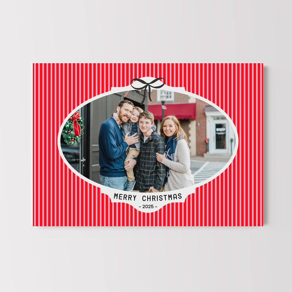 Holiday card with a red and pink striped background, white oval framed photo, black bow and text. 