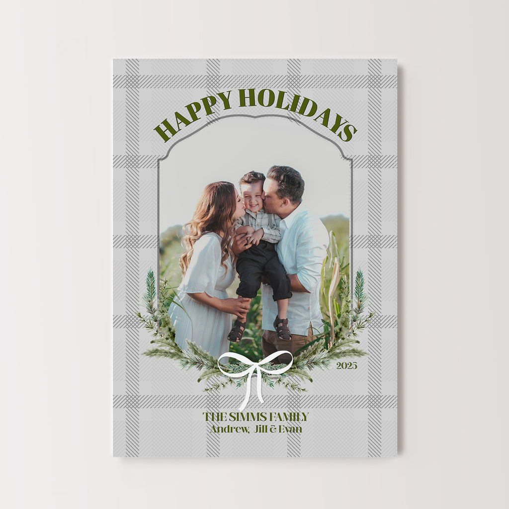 holiday card template with a photo framed in evergreen branches and a white bow on a gray plaid background with green text