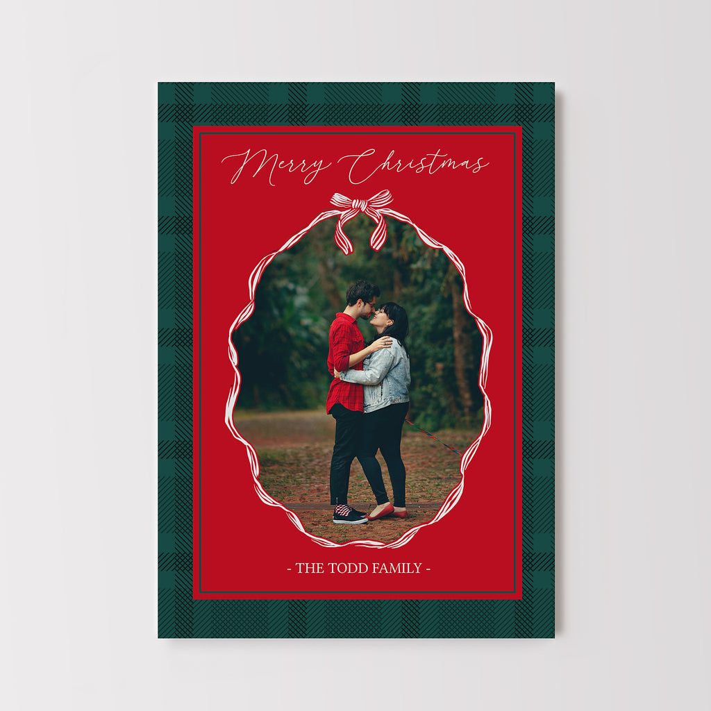 Christmas card in classic red and green colors with a plaid background, elegant fonts and a red ribbon oval shaped photo frame.