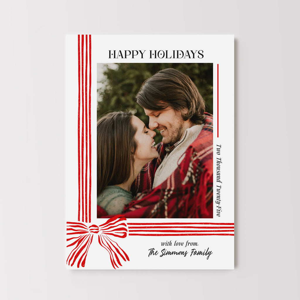 Christmas card in a vertical format with a portrait photo on a white background with a red striped ribbo and bow with black text. 