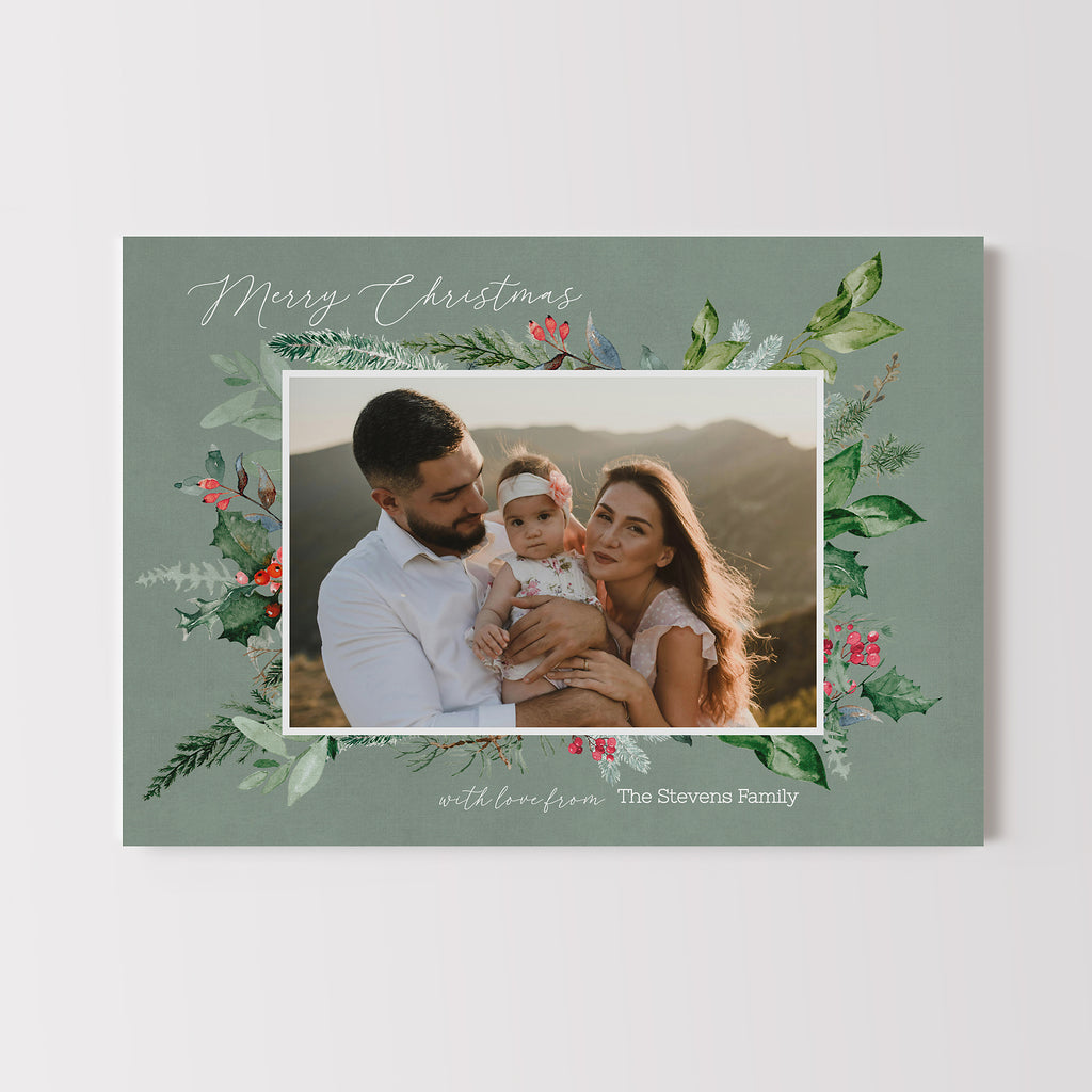 Holiday card featuring a single family photo framed with winter greenery on a soft light green background.