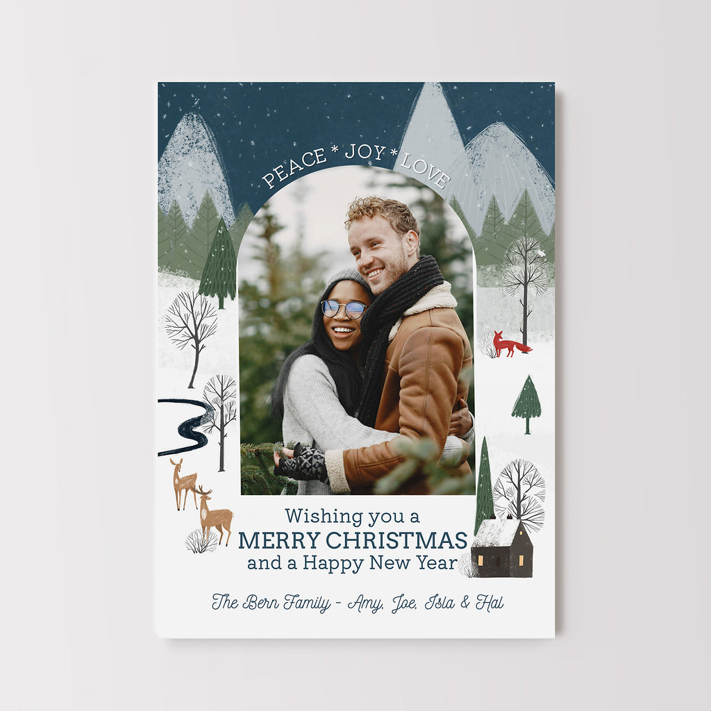 Christmas card with an arched photo in center and winter woodland scene in background. 